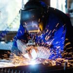 Welder using welding equipment with sparks flying in workshop, representing welding supplies and tools in Canada