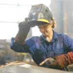 Person wearing protective welding gear using welding accessories and safety equipment while working on a metal fabrication project in a garage workshop.
