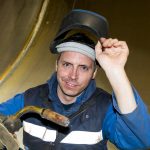 Welder holding a MIG welding gun and lifting his welding helmet