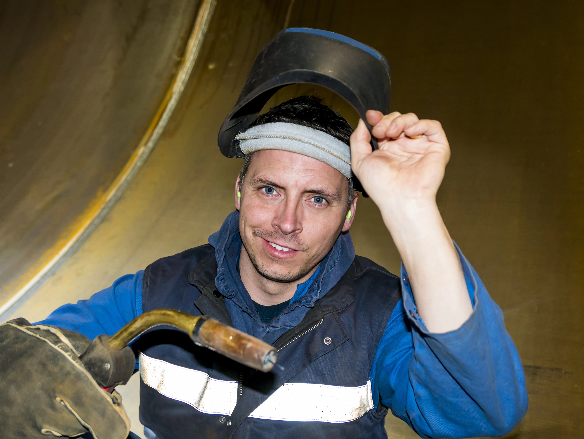 Welder holding a MIG welding gun and lifting his welding helmet